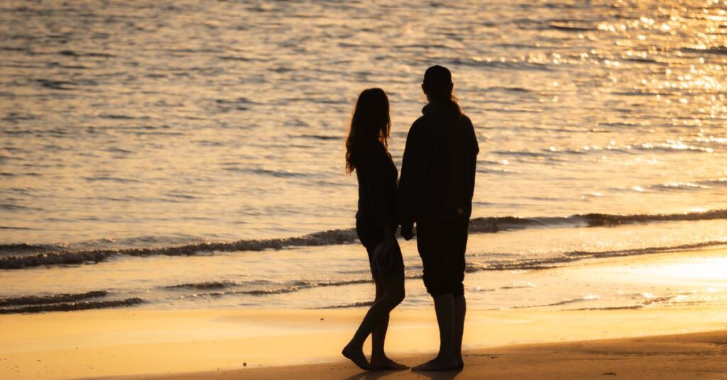 Three of us ending explained: couple walking on a quiet coastal beach